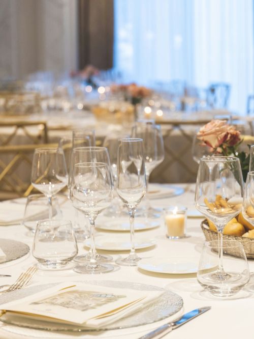 A beautifully set table with elegant glassware, roses, candles, and a basket of bread, set in an upscale dining environment.