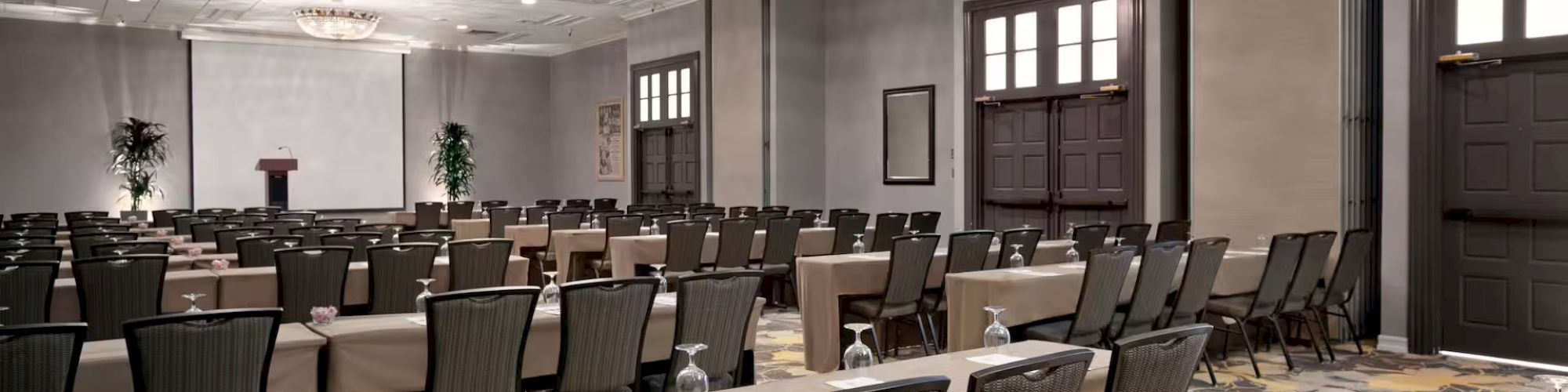 An empty conference room with rows of chairs and tables, a podium, and a projector screen at the front, ready for a meeting.