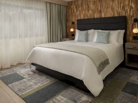 A modern hotel bedroom with a king bed, neutral palette, patterned rug, and matching nightstands flanking the headboard, soft ambient lighting.