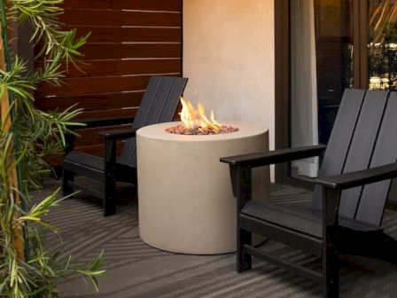 A cozy outdoor seating area with two dark wooden chairs surrounding a circular fire pit, on a wooden deck with greenery nearby.