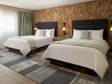 A modern hotel room with two neatly made twin beds, wood-paneled accent wall, and soft lighting, creating a calm, contemporary vibe.